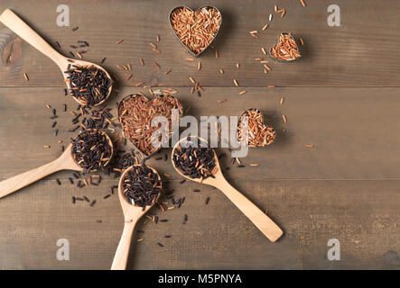 Reihe von Braun jasmin Reis mit verschiedenen Reis: Reis Berry und Thai Red Gemischter Reis auf braunem Holz- Hintergrund, organischen Reis und gesundes Essen. Stockfoto