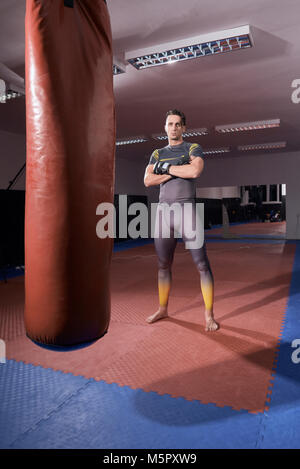 Einen jungen Boxer stehend posiert, an der Kamera schaut. voller Länge geschossen. drinnen, Boxsack. Stockfoto