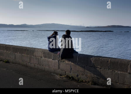 Zwei junge Mädchen sitzen an einer Wand mit Blick aufs Meer Stockfoto