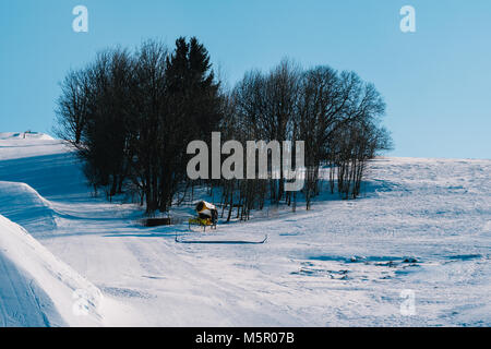 Schneekanone auf der Skipiste im Winter. Eine Menge Schnee herum. Blauer Himmel ohne Wolken. Es gibt keine Personen, die am Hang. Stockfoto