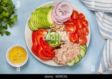 Thunfischsalat, Quinoa und Gemüse: Gurke, Avocado, Paprika, Tomaten, Petersilie auf einer weißen Platte auf einem blauen Hintergrund. Blick von oben. Buddha Stockfoto