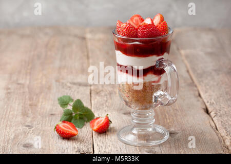 Käsekuchen mit Erdbeeren in einem Glas auf den alten hölzernen Hintergrund Stockfoto