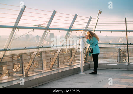 Minsk, Weißrussland. Junge Frau von Münzautomaten Teleskop Suchen aus Sicht Plattform auf der Nationalbibliothek. Stockfoto