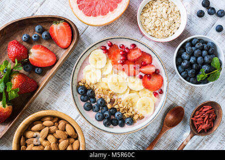 Smoothie Schüssel mit Bananenscheiben, Erdbeere, Heidelbeere, Müsli und Granatapfel Samen. Ansicht von oben. Gesunde Lebensweise, gesunde Ernährung, Diäten, Gewicht Stockfoto