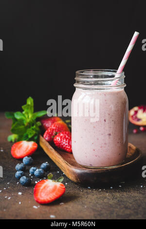 Strawberry Smoothie in ein Glas mit Strohhalm auf dunklem Hintergrund. Kopieren Sie Platz für Text, vertikale Zusammensetzung Stockfoto