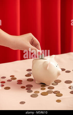 Eine weibliche Hand halten eine Münze, und setzen Sie sie in Schwein coin Bank Stockfoto