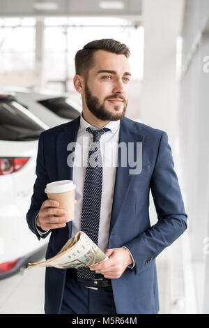 Portrait von gut aussehenden bärtigen Geschäftsmann während der kaffeepause stehen durch Fenster in modernen Büro Stockfoto