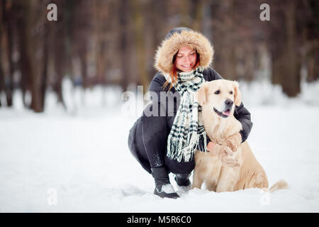Foto von Mädchen in schwarzen Jacke hocken neben Hund im Winter Stockfoto