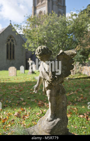 Eine steinerne Statue eines Cherubs auf einem Grab auf dem Friedhof von St. Maria, der Jungfrau, Kirche, Huish Episcopi, in der Nähe von Langport in Somerset, England Stockfoto