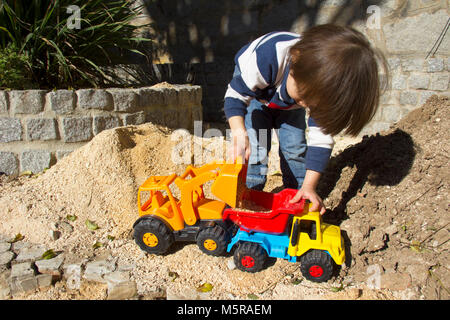 Wenig drei Jahre alten Jungen spielen im Sand mit einem Bagger und Kipper. Stockfoto