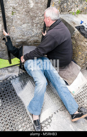Ein Besucher legt Zurück zu den Blarney Stone Küssen mit Hilfe von einem Mitarbeiter an der Oberseite des Blarney Castle in Blarney Castle im Süden Irlands Stockfoto