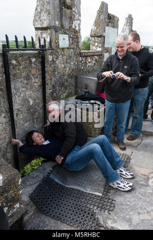 Ein Besucher legt Zurück zu den Blarney Stone Küssen mit Hilfe von einem Mitarbeiter an der Oberseite des Blarney Castle in Blarney Castle im Süden Irlands Stockfoto
