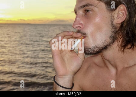 Nahaufnahme einer jungen kaukasischen Mann Rauchen einer Zigarette am Strand. Stockfoto