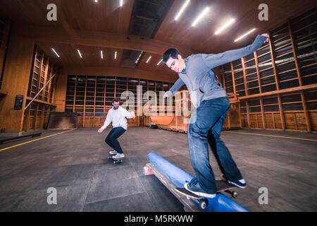 Zwei junge Skater sind sie Tricks mit ihren Skateboards in einen Indoor skate Hall. Stockfoto