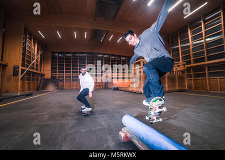 Zwei junge Skater sind sie Tricks mit ihren Skateboards in einen Indoor skate Hall. Stockfoto