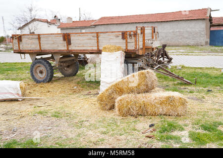 Mehrere Strohballen neben dem Traktor Anhänger und Landhäuser und Heuboden im Hintergrund Stockfoto