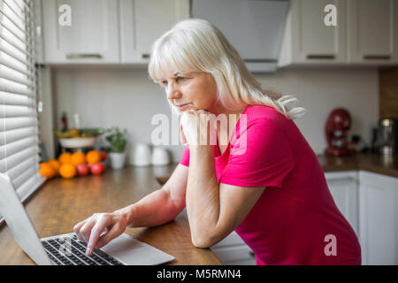 Portrait der älteren Dame mit Laptop auf den Küchentisch Stockfoto
