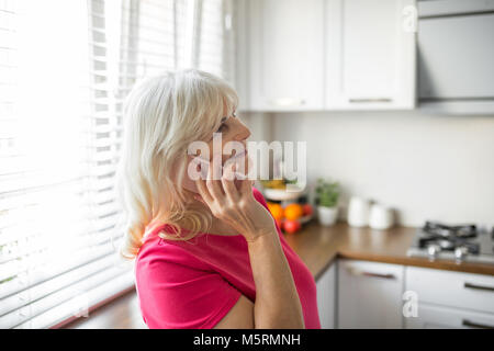Profil Portrait von gerne ältere Dame sprechen auf Mobile in der Küche Stockfoto