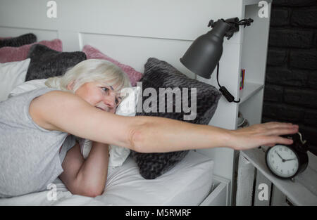 Portrait der älteren Dame im Bett Wecker ausschalten Stockfoto