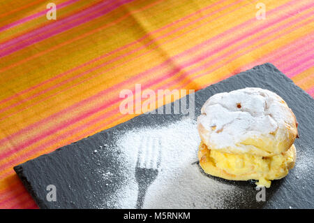 Saint John's Windbeutel auf schiefer Platte, mit lecker Sahne mit Zucker auf bunten Tischdecke gefüllt Stockfoto