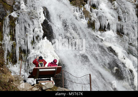 25. Februar 2018, Deutschland, Todtnau: Ausflügler sitzen auf einer Bank auf dem teilweise gefrorenen Todtnauer Wasserfälle suchen. Die todtnauer Wasserfall im südlichen Schwarzwald ist einer der höchsten Wasserfälle in Deutschland. Foto: Steffen Schmidt/dpa Stockfoto