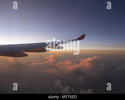 Luftbild vom Flugzeug, das Flugzeug Flügel und rosa Sonnenuntergang Licht von der linken Seite, über Wolken Horizont unter blauem Himmel, dunkel ist Stockfoto