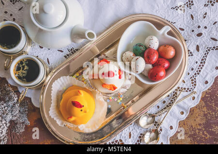 Figuren aus Marzipan in Form von weißen und gelben Hühner auf Ostern Tisch mit Kaffeetassen und Gebäck Eier in einem Ceramic White pot. Close Up. Stockfoto