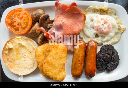 Englisches Frühstück Spiegelei, Speck, Bohnen, weiße Muffin, Blutwurst, Grilltomate, Würstchen, Pilze und Hash Browns Stockfoto