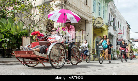 PENANG, MALAYSIA, 12.November 2017, traditionelle Rikscha und eine Gruppe von Touristen auf dem Fahrrad in den Straßen von George Town. Stockfoto