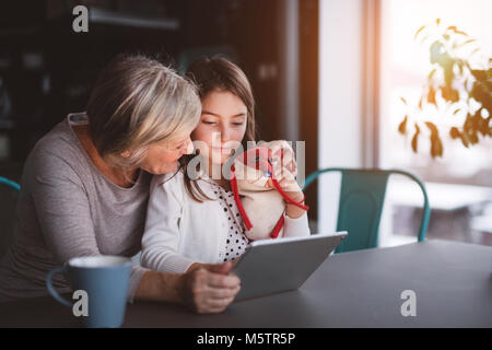 Ein kleines Mädchen und Großmutter mit Tablet-PC zu Hause. Stockfoto