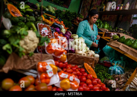 Ein kolumbianischer Anbieter packs frisches Gemüse in einer Plastiktüte auf dem Markt der Paloquemao in Bogotá, Kolumbien. Stockfoto
