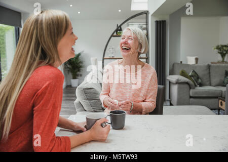 Ältere Frau genießt ein Aufholen mit ihrer Tochter. Sie sitzen in der Küche trinken Tassen Tee. Stockfoto
