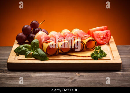 Käse und Schinken auf Schneidebrett auf hölzernen Tisch Stockfoto