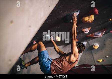 Athletischer mann Bouldern in einer Kletterhalle. Professioneller Kletterer an der Wand den Kopf Klettern in der Kletterhalle. Stockfoto