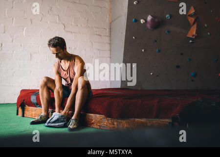 Mann, der an einer Wand Kletterhalle Anwendung magnesium Chalk Pulver auf die Hände aus der Tasche. Künstliche bouldern Wand im Hintergrund. Stockfoto