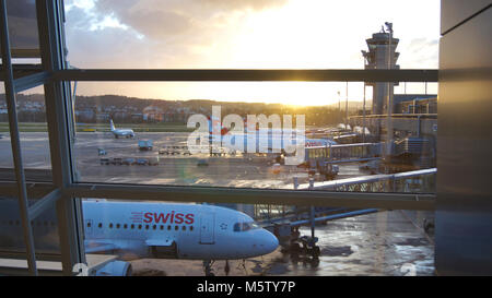 Zürich, Schweiz - Mar 31, 2015: Blick auf den Flughafen durch das Fenster der Wartebereich - Flugzeuge der Schweizer Fluggesellschaft in einer Reihe vor den Toren bei Sonnenschein Stockfoto