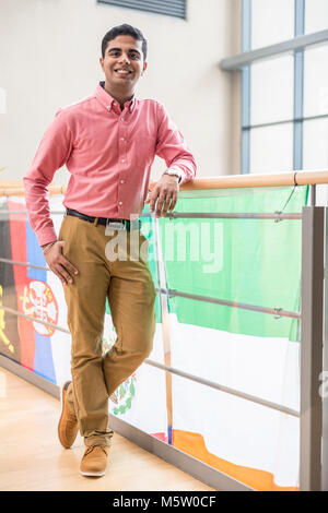 Ein männlicher zuversichtlich International Student steht auf dem Campus mit Fahnen hinter ihm an einer Universität/Hochschule Stockfoto