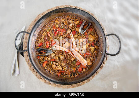 Ein Blick von oben auf eine traditionelle Paella mit Meeresfrüchten, die in einer rustikalen Pfanne serviert wird, mit Garnelen, Muscheln und gemischtem Gemüse auf einem Bett mit Safranreis Stockfoto