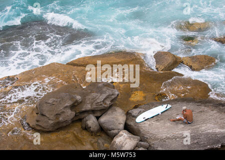 Mann auf Felsen an Nähe: Tamarama Beach, Sydney, New South Wales, Australien sitzen Stockfoto