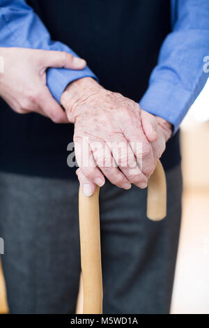 Der ältere Mann die Hände auf Gehstock mit Sorgfalt Arbeiter im Hintergrund Stockfoto
