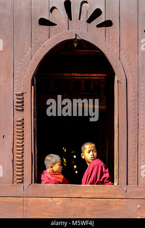 Zwei junge Mönche sind aus einem ovalen Fenster Shwe Yaunghwe Kyaung Kloster Stockfoto