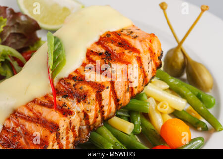 Gegrilltes Lachsfilet mit Hollandaise-Sauce, grünen Bohnen, Karottengarnitur und Limette, serviert auf einem eleganten Restaurantteller. Stockfoto