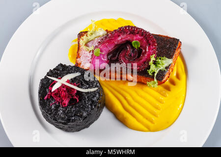 Gourmet-Lachs mit Oktopus, schwarzem Reis und gelber Sauce, Feinschmeckerpräsentation. Stockfoto
