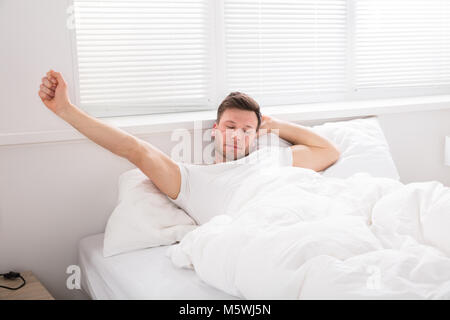 Ein junger Mann seine Hände ausstrecken nach dem Aufwachen im Bett am Morgen Stockfoto