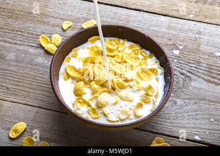 In einem Ton Schüssel mit Cornflakes gießen Milch. Die Platte steht auf einem Holz- Oberfläche. Stockfoto