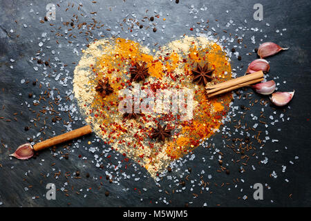 Herzform aus Gewürzen mit Zimt und Knoblauch Pfeil auf schiefer Hintergrund Stockfoto