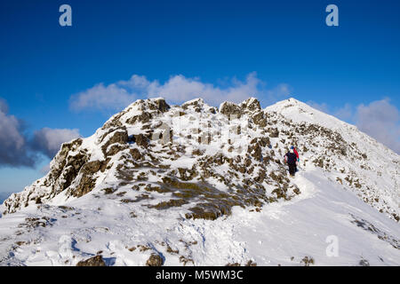 Wanderer Wandern Down South Ridge auf Menai Bridge vom Gipfel des Mt Snowdon Gipfel mit Schnee im Winter in Snowdonia National Park. Gwynedd North Wales UK Stockfoto