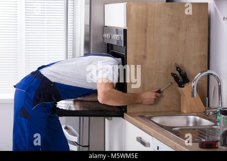 Junge männliche Elektriker Instandsetzung Ofen mit einem Schraubendreher in der Küche Stockfoto