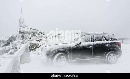 Schwarze Familie Auto auf einem schneebedeckten Berggipfel. Frostig winterliche Szene mit der sport utility vehicle stehen innerhalb einer Wolke auf dem Berg. Stockfoto