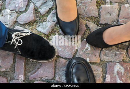 Vier Füße in formelle Schuhe auf Kopfsteinpflaster. Ansicht von oben. Close-up Männliche und weibliche Beine gemeinsam auf alte Pflasterung. Teamwork, Motivation oder Verschwörung. Stockfoto